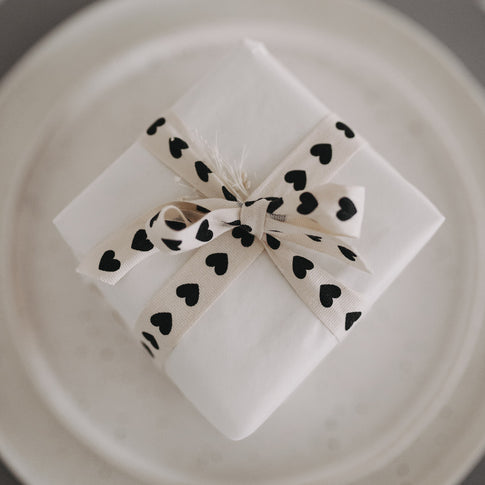 Kleines Geschenk mit Geschenkband mit schwarzen Herzen auf Teller.