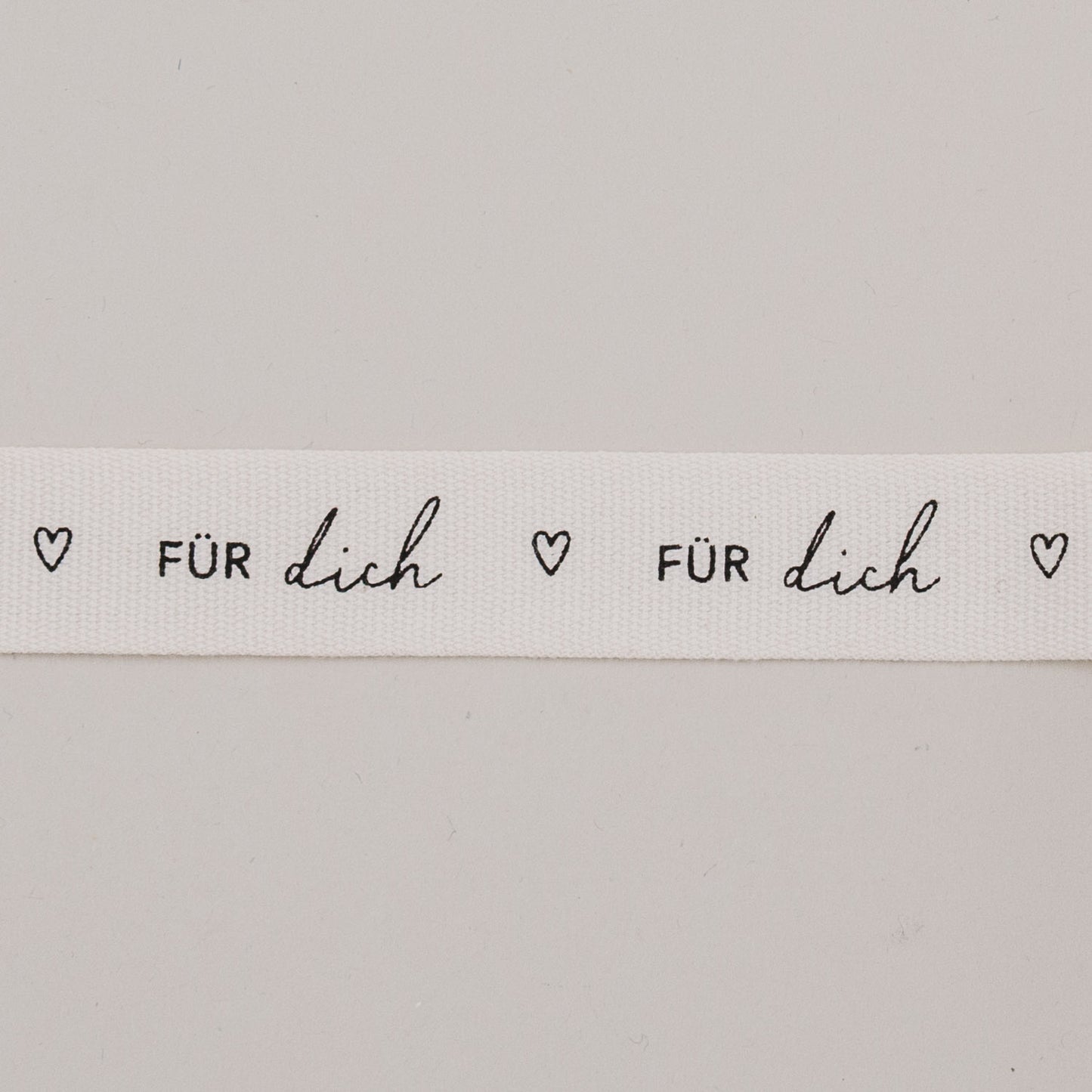 Detailaufnahme vom Geschenkband „Für dich“ mit Herzen, schwarzer Schrift auf weißem Baumwollband.