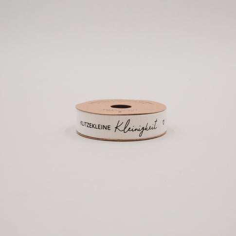 Seitliche Ansicht der Geschenkbandrolle „Klitzekleine Kleinigkeit“ mit schwarzem Schriftzug auf Naturband