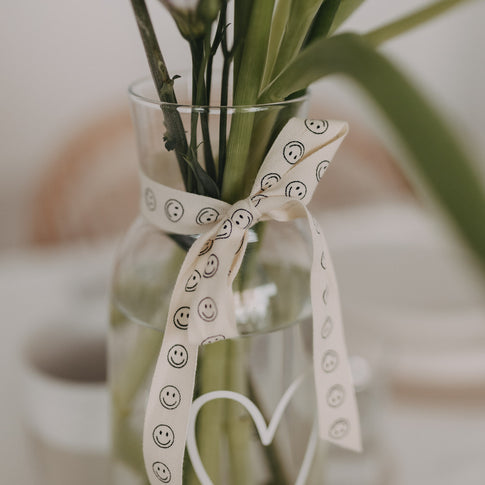 Vase mit Blumen, gebunden mit cremefarbenem Smiley-Geschenkband.