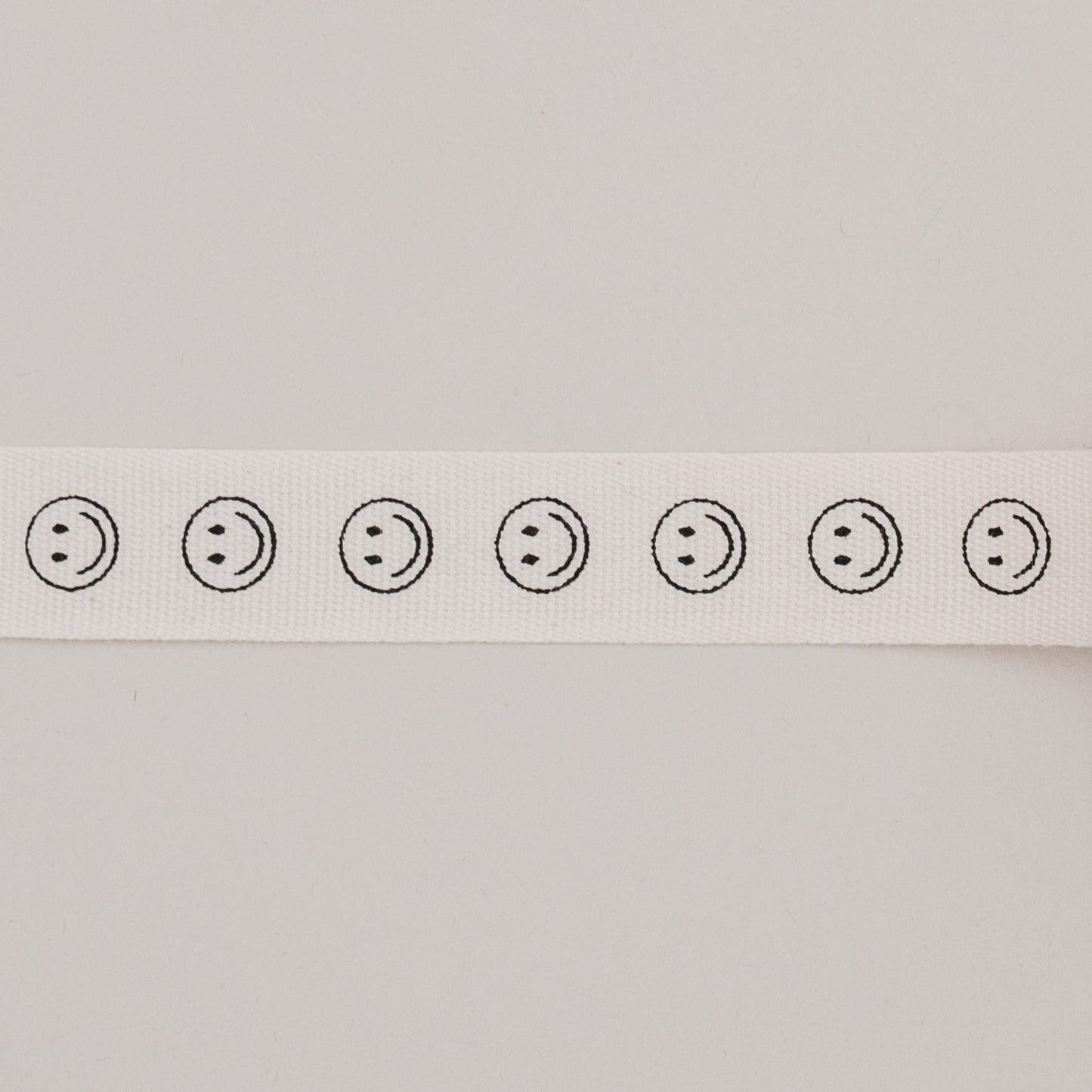 Nahaufnahme des Geschenkbandes Smileys, zeigt schwarze Smileymotive in Reihe auf naturweißem Baumwollband