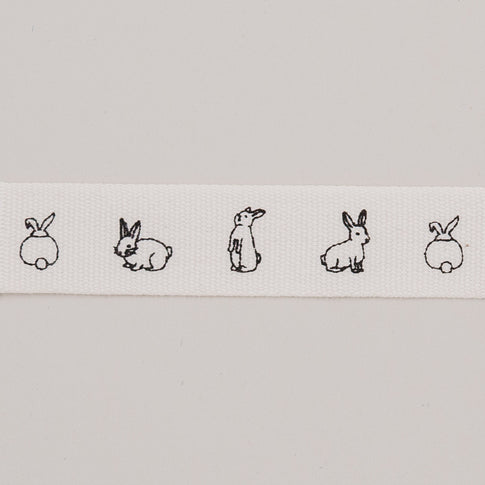 Nahaufnahme des weißen Geschenkbandes mit feinen schwarzen Kaninchenzeichnungen.