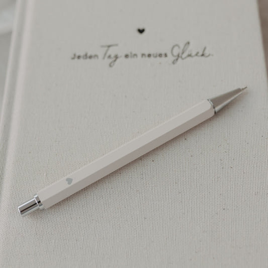 Druckbleistift Creme auf Notizbuch mit feiner Struktur und Herzmotiv.