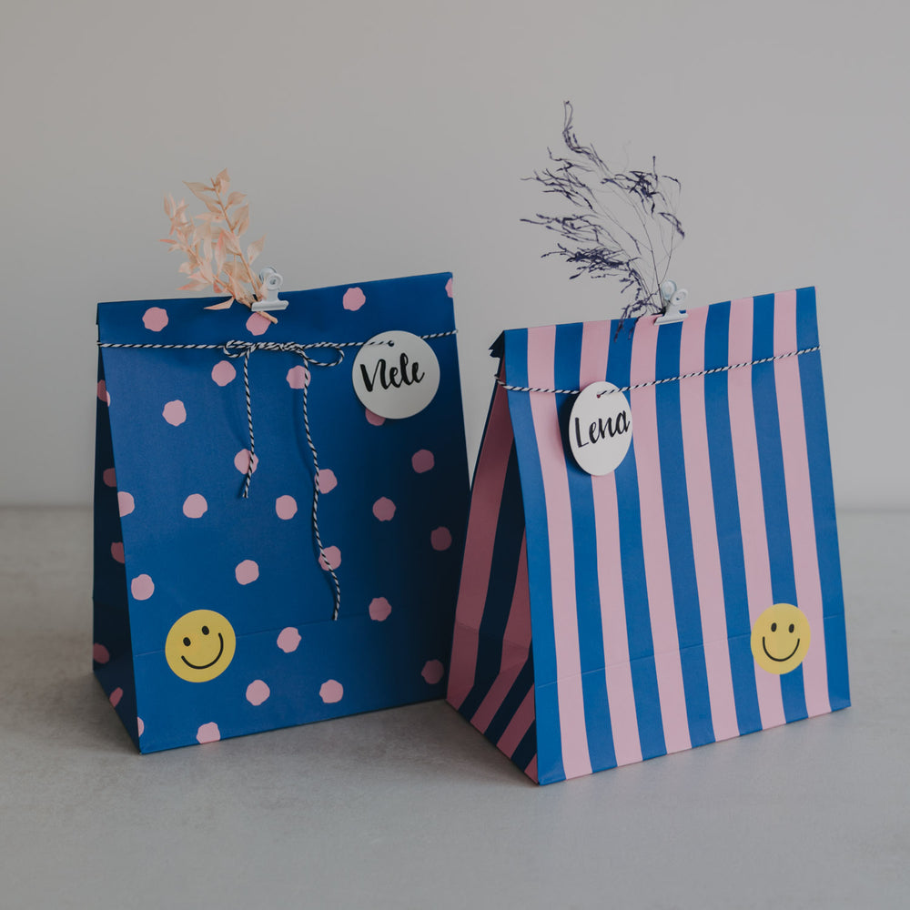 Papier-Geschenktüten in Blau und Rosa mit Streifen und Punkten, fröhliches Design mit Namensanhängern.