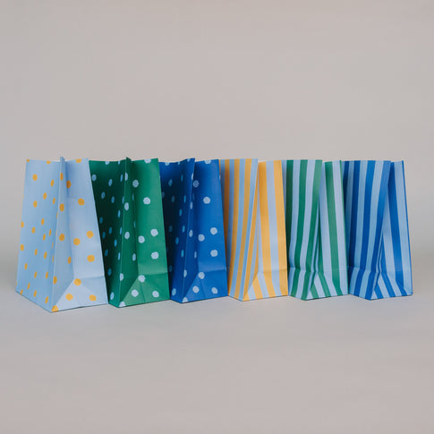 Mehrere Papier-Geschenktüten in Blau, Grün und Gelb von der Seite nebeneinander