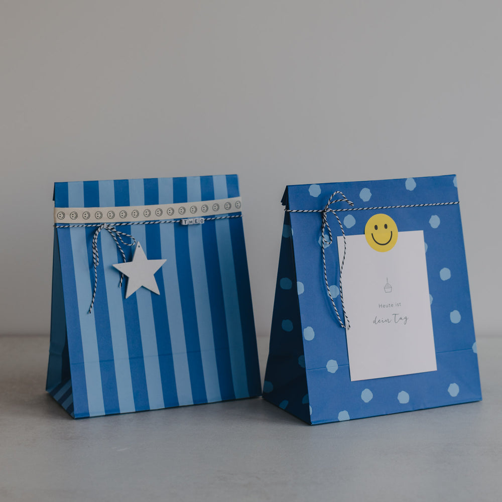 Zwei blaue Papier-Geschenktüten mit Streifen und Punkten, mit Anhängern dekoriert