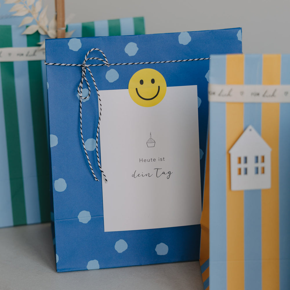 Blaue Papier-Geschenktüte mit Punkten und Geschenkanhänger mit Smiley