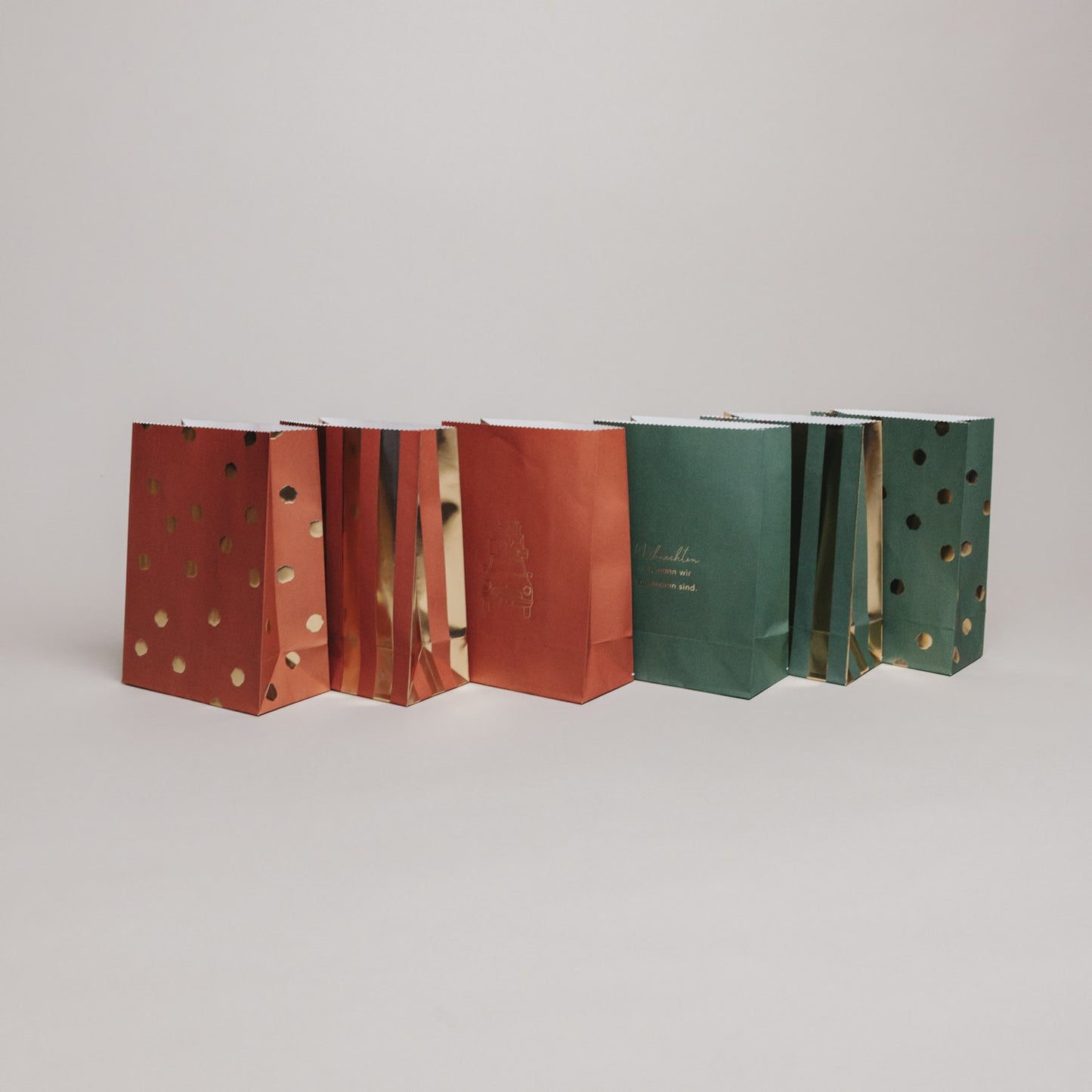 Rückansicht weihnachtlicher Geschenktüten aus Papier in Grün und Rot mit goldenen Akzenten