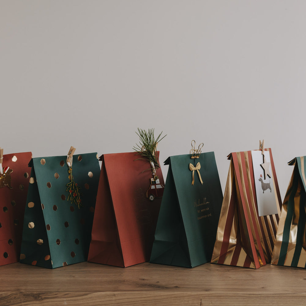 Seitliche Ansicht mehrerer Papiergeschenktüten in Grün und Rostrot mit weihnachtlichen Mustern