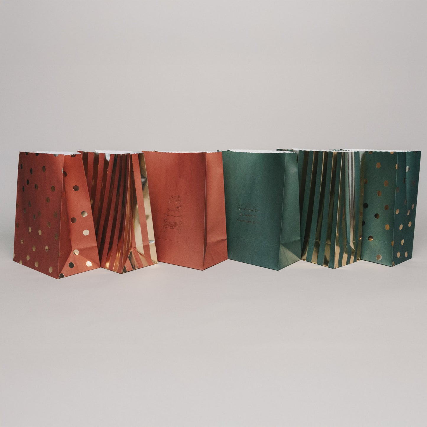 Rückansicht verschiedener Papiergeschenktüten im Weihnachtsdesign, aufgereiht vor hellem Hintergrund