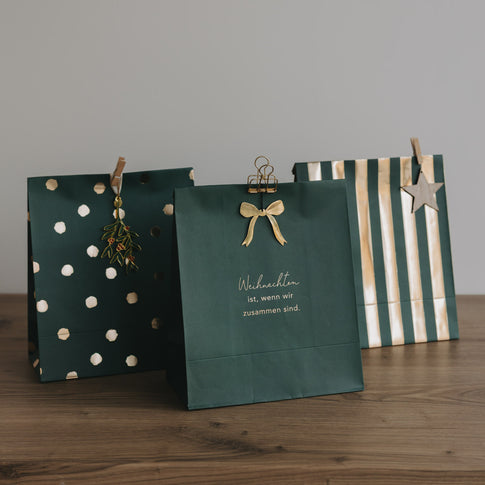 Weihnachtliche Papiergeschenktüten in Dunkelgrün mit Goldakzenten und Schriftzug, auf Holzfläche