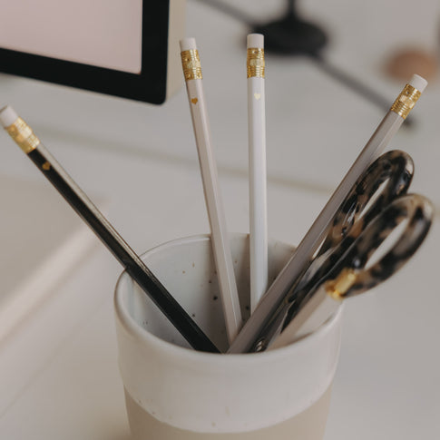 Bleistifte in Creme, Weiß und Schwarz mit goldenen Details in Becher neben Schere
