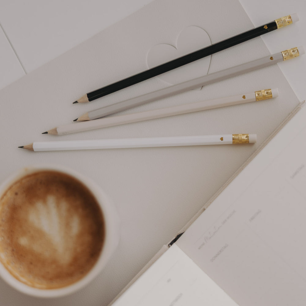 Vier Bleistifte in Creme, Weiß und Schwarz auf Notizbuch mit Herzprägung