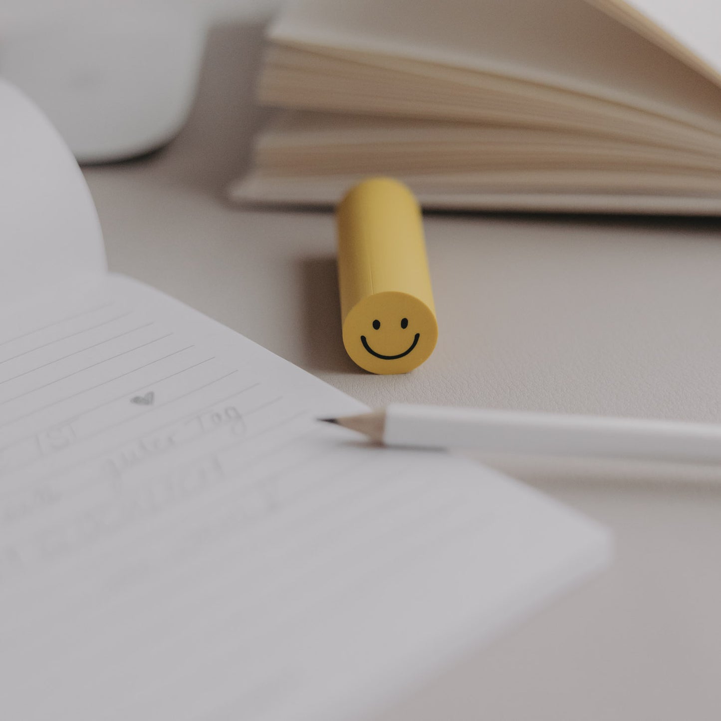Radiergummi Smiley in Gelb auf Schreibtisch neben Notizbuch und Stift