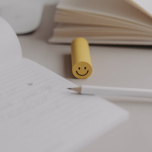 Radiergummi Smiley in Gelb auf Schreibtisch neben Notizbuch und Stift