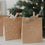 Geschenktüten aus Kraftpapier mit „Frohe Weihnachten“ und Tannenbaum-Motiv vor Weihnachtsbaum