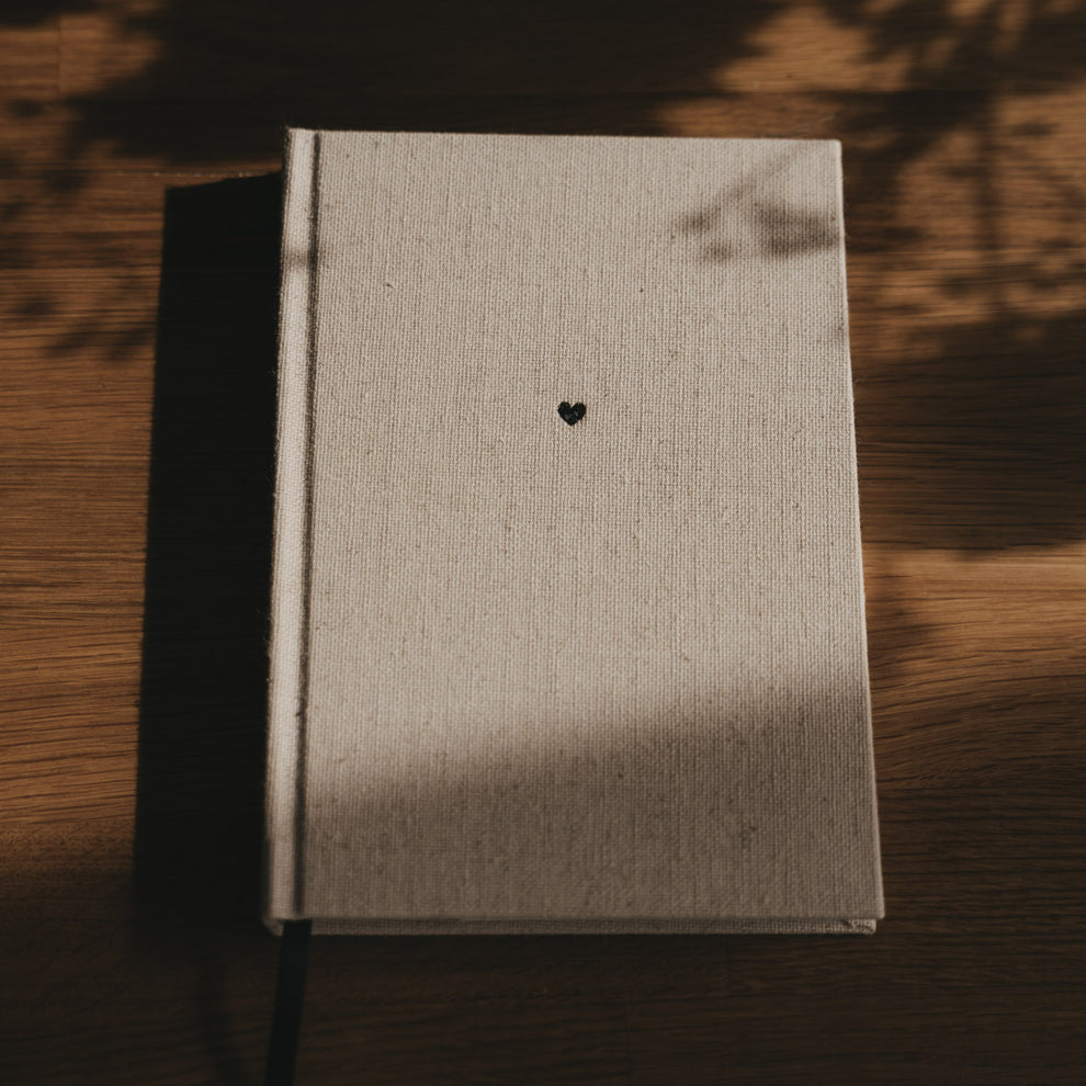 Gepunktetes A5 Notizbuch mit beigem Stoffeinband, schwarzem Herz und Leseband auf Holztisch